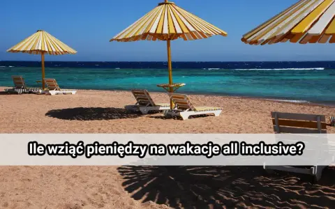 Plaża z leżakami i parasolami pod żółto-białymi pasami, turkusowe morze i błękitne niebo.