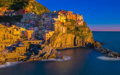 Kolorowe domy Cinque Terre w **Włoszech we wrześniu**, oświetlone złotym słońcem, schodzą ku morzu.