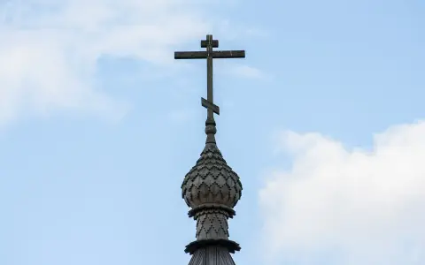 Drewniany krzyż prawosławny na tle błękitnego nieba z chmurami.