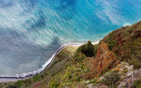 Widok z góry na klif Madery, pola uprawne i ocean.