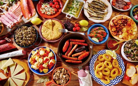 Tapas co to? Obficie zastawiony stół pełen hiszpańskich przekąsek: kiełbaski, krewetki, kalmary, owoce morza, sery, wędliny i tortilla.