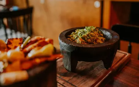 Świeże guacamole w kamiennym moździerzu, obok talerza z innymi najpopularniejszymi daniami meksykańskimi.