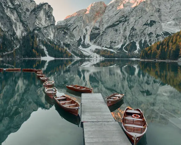 Drewniane łodzie przy drewnianym pomoście na spokojnym Lago di Braies, odbijające się w tafli wody, z majestatycznymi górami w tle.