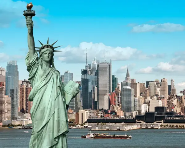 Statua Wolności wita podczas podróży do USA. W tle panorama Nowego Jorku z drapaczami chmur i statkami na rzece.