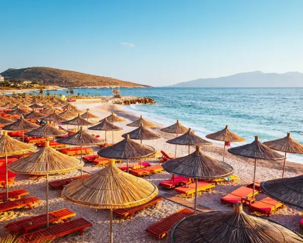 Albania, lipiec: słoneczna plaża z rzędami parasoli i leżaków, turkusowe morze i góry w tle. Idealna pogoda na wakacje.