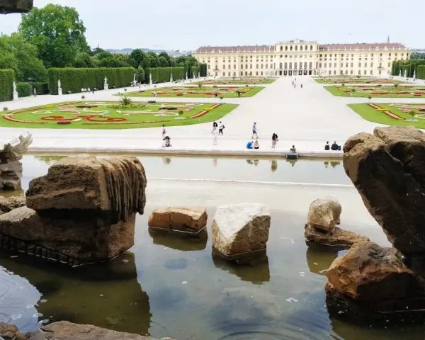 Wiedeń ogrody Sisi: malowniczy widok na pałac Schönbrunn i jego kwieciste tarasy, z kamienną fontanną w pierwszym planie.