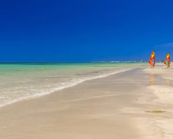 Piękna, słoneczna plaża w Tunezji. Idealna pogoda w maju na windsurfing, o czym świadczą trzy kolorowe żagle na piasku.