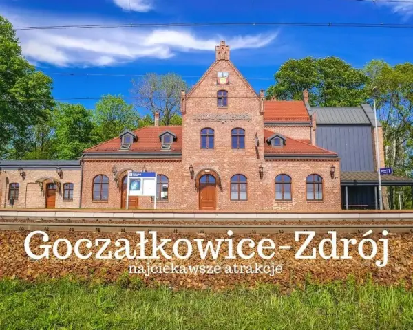 Ceglana stacja kolejowa Goczałkowice-Zdrój z czerwonym dachem i zielonymi drzewami w tle.