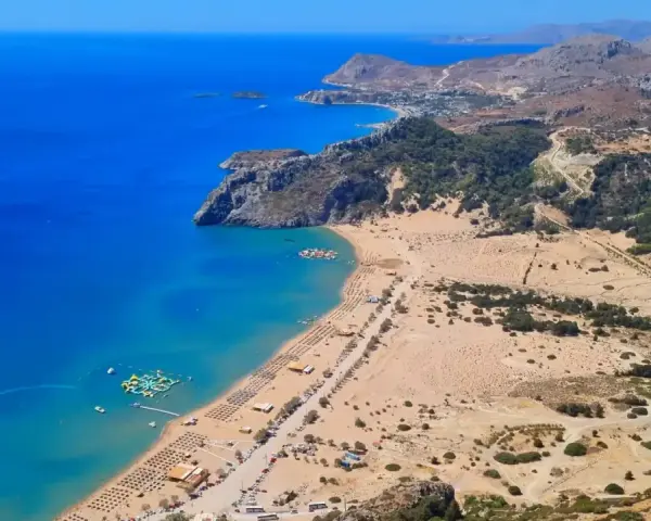 Widok z lotu ptaka na piaszczystą plażę z leżakami, turkusowe morze i górzysty krajobraz Rodos.