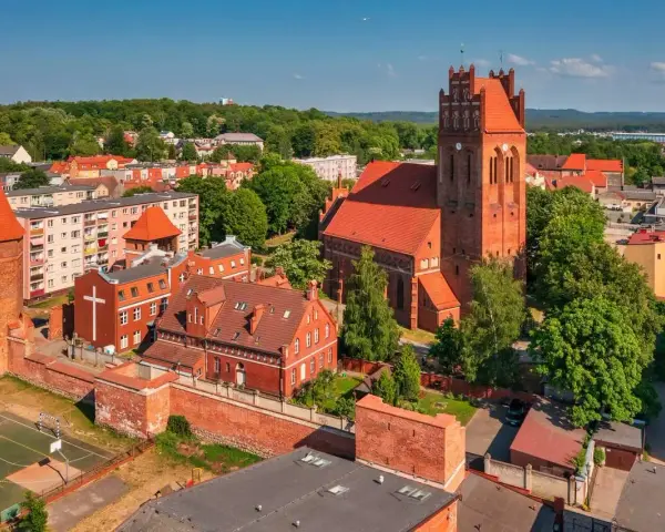 Zamek krzyżacki w Lęborku, z charakterystyczną wieżą i ceglaną architekturą, otoczony zielenią i zabudowaniami miejskimi.