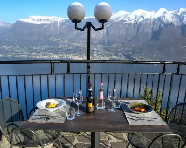Stół z winem i jedzeniem na tarasie z widokiem na jezioro i ośnieżone góry. Idealne miejsce na romantyczną kolację z widokiem, prawdziwa "terrazza del brivido".