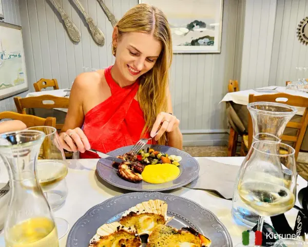 Szukasz miejsca, gdzie zjeść w Wenecji? Uśmiechnięta kobieta delektuje się daniem z ośmiornicy i warzywami w urokliwej restauracji.