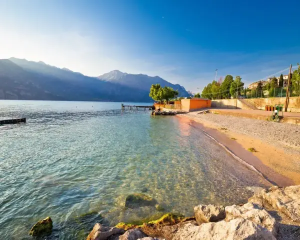Słoneczna plaża nad jeziorem Garda z kamienistym brzegiem i łagodnymi falami.
