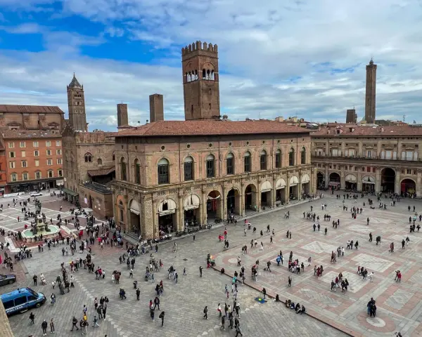Plac Maggiore w Bolonii z wieżami i tłumem ludzi.