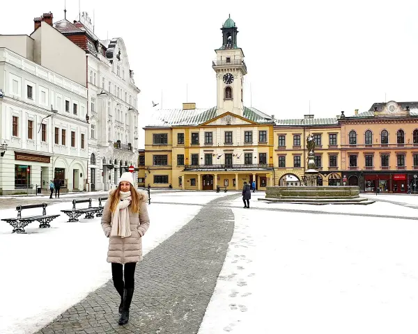 Zimowy spacer po Rynku w Cieszynie. Kobieta w ciepłym ubraniu przemierza ośnieżony plac, podziwiając zabytkowe kamienice i ratusz. Idealny pomysł na cieszyn w jeden dzień.