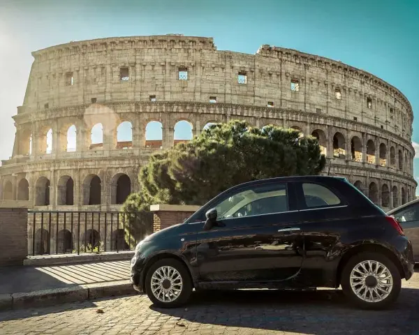 Czarny Fiat 500 pod Koloseum w Rzymie. Zastanawiasz się, ile się jedzie z Polski do Włoch samochodem?