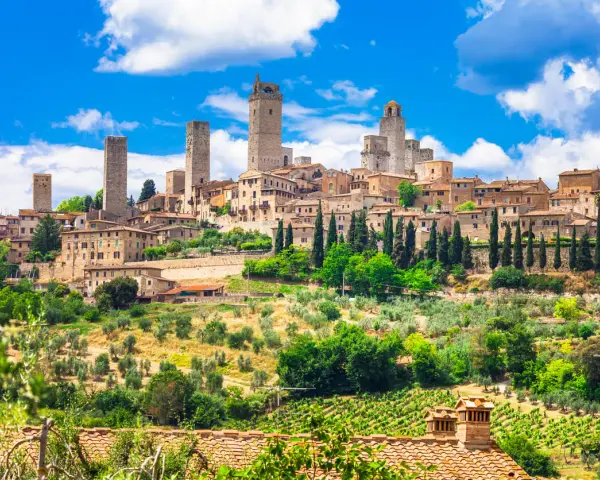 Widok na średniowieczne wieże i zabudowania San Gimignano w Toskanii, otoczone zielenią i winnicami.