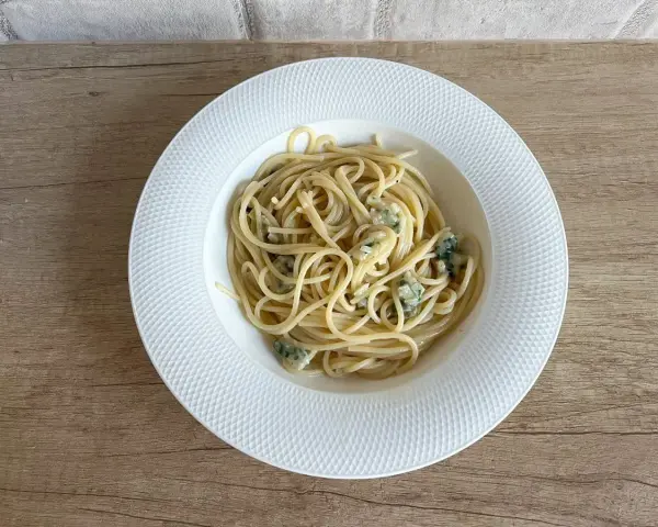 Pyszne spaghetti aglio olio z kawałkami sera pleśniowego na białym talerzu.