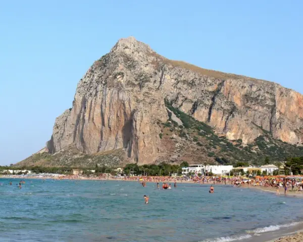 Słoneczna plaża w San Vito Lo Capo, z turkusową wodą i majestatyczną górą w tle. Tłumy ludzi cieszą się wakacjami.
