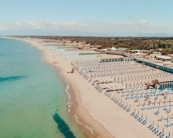 Widok z lotu ptaka na plażę w Marina di Cecina, Toskania, z rzędami leżaków i parasoli.