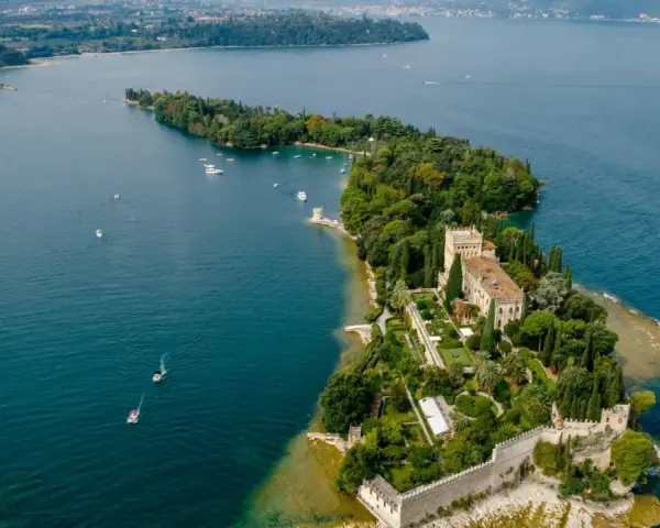 Malowniczy widok na Isola del Garda z pałacem i ogrodami, otoczony turkusową wodą jeziora.