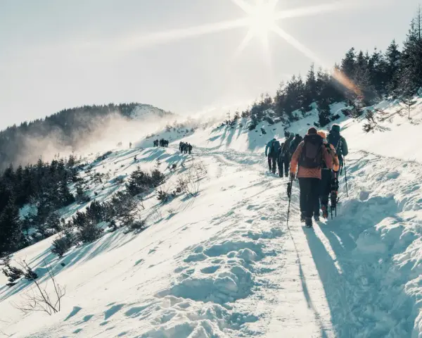 Grupa turystów wędruje ośnieżonym szlakiem w Tatrach pod jasnym słońcem.