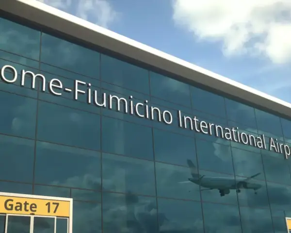 Lotnisko Rzym Fiumicino. Jak dojechać do centrum? Widok na nowoczesny budynek lotniska z napisem "Rome-Fiumicino International Airport" i odbijającym się samolotem.
