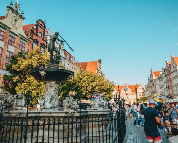 Fontanna Neptuna na tle kamienic i tłumu ludzi w Gdańsku.