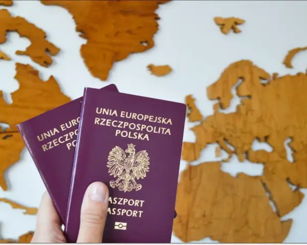 Dwa polskie paszporty w dłoni na tle drewnianej mapy świata. Planujesz podróż? Dowiedz się, jak wyrobić paszport.