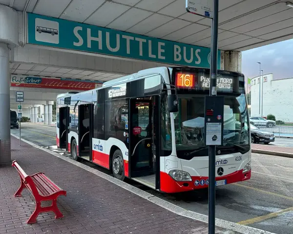 Autobus wahadłowy z lotniska do centrum miasta, z otwartymi drzwiami, gotowy do odjazdu.