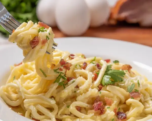 Pyszne spaghetti carbonara przepis na talerzu, z widocznymi jajkami i boczkiem w tle. Idealne danie dla miłośników włoskiej kuchni.