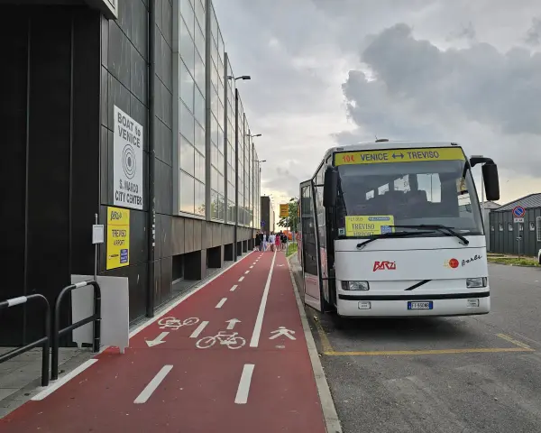 Autobus z napisem "Venice Treviso" czeka na pasażerów przy lotnisku. Obok czerwona ścieżka rowerowa i piesza.