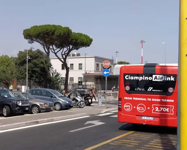 Czerwony autobus Ciampino Airlink na tle parkingu i budynków.