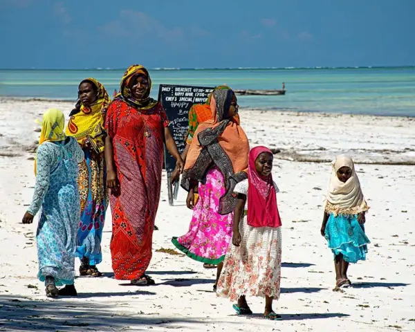 Kobiety w kolorowych strojach spacerują po plaży Zanzibaru. Warto wiedzieć, że to miejsce oferuje piękne widoki i lokalną kulturę.