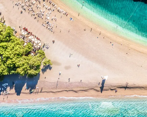 Chorwacja plaże piaszczyste, z turkusową wodą i zielonymi drzewami. Leżaki i parasole czekają na plażowiczów.