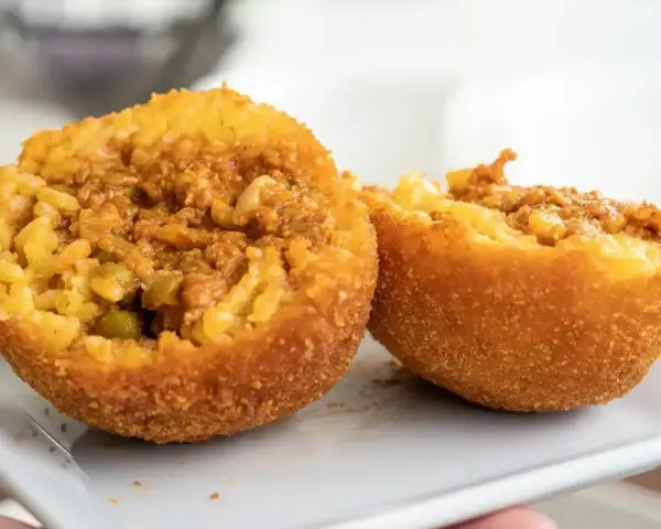 Arancini co to? Chrupiące kulki ryżowe z mięsnym farszem i groszkiem, przekrojone na pół, prezentują swoje bogate wnętrze.