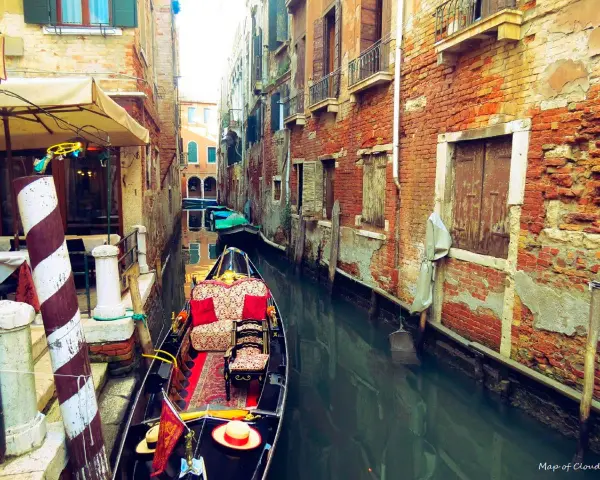Gondola z czerwonymi poduszkami i dywanem w wąskim kanale Wenecji, otoczonym starymi ceglanymi budynkami.