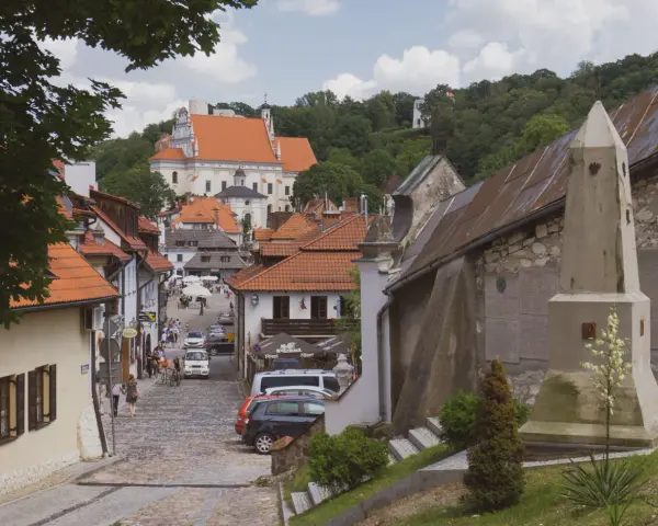 Widok na urokliwą, brukowaną uliczkę Kazimierza Dolnego z zabytkową architekturą i kościołem w tle.