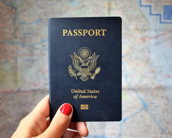 Dłoń trzyma paszport USA na tle mapy. Czas oczekiwania na paszport może być długi, ale podróż warta jest tej chwili.