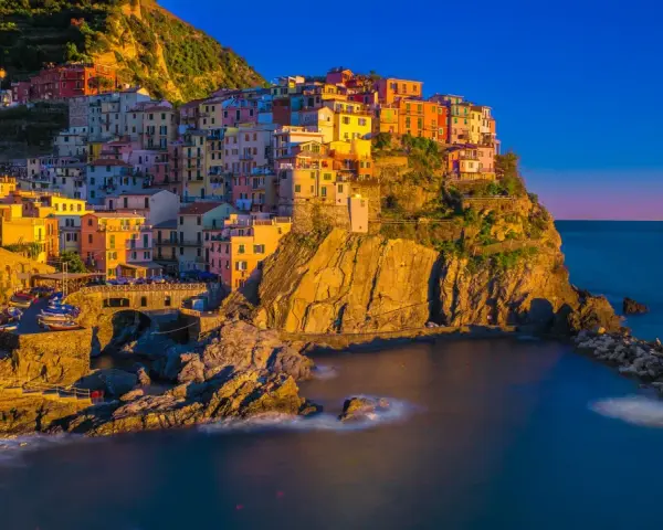 Kolorowe domy Cinque Terre w **Włoszech we wrześniu**, oświetlone złotym słońcem, schodzą ku morzu.