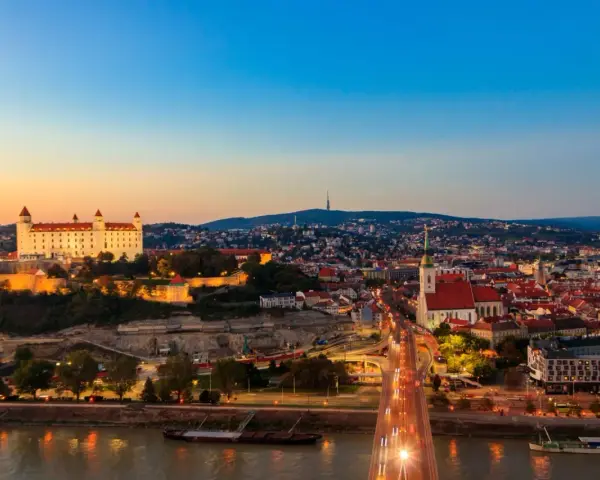 Widok na Bratysławę o zachodzie słońca z zamkiem i mostem nad Dunajem.