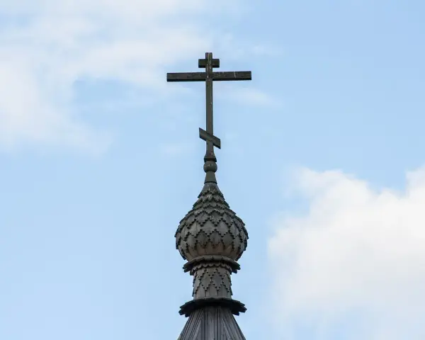 Drewniany krzyż prawosławny na tle błękitnego nieba z chmurami.