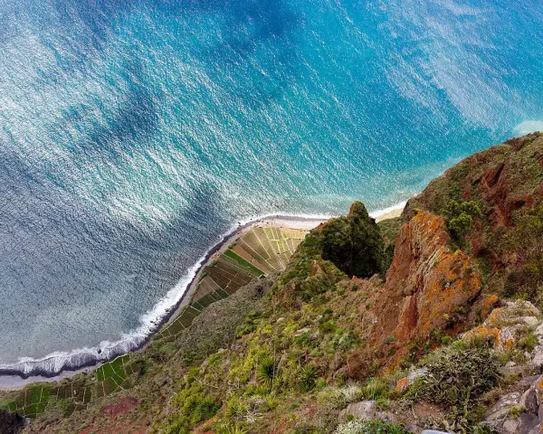 Widok z góry na klif Madery, pola uprawne i ocean.