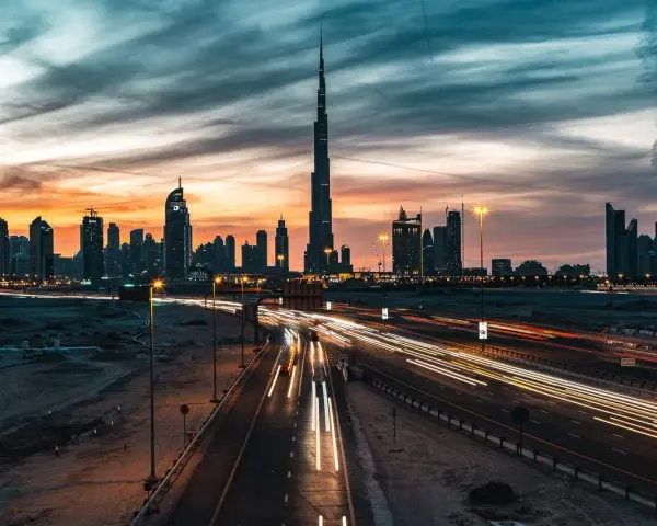 Wieczorny widok na Dubaj z Burj Khalifa, gdzie światła samochodów tworzą smugi na autostradzie. Ciekawostki o tym drapaczu chmur mogą dotyczyć jego wysokości i budowy.