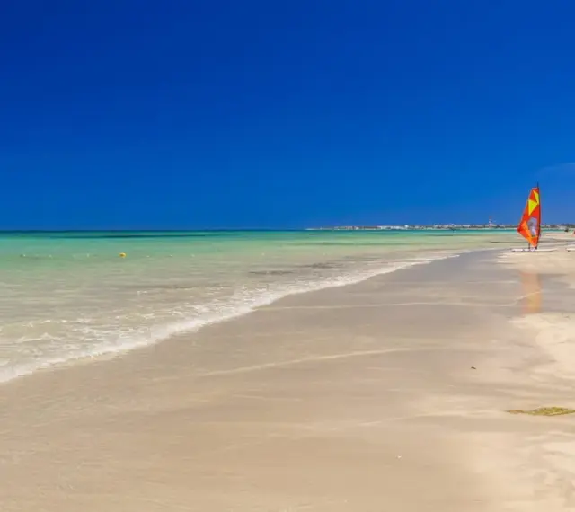 Piękna, słoneczna plaża w Tunezji. Idealna pogoda w maju na windsurfing, o czym świadczą trzy kolorowe żagle na piasku.