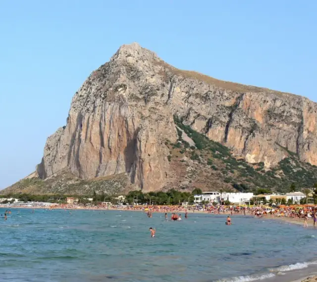 Słoneczna plaża w San Vito Lo Capo, z turkusową wodą i majestatyczną górą w tle. Tłumy ludzi cieszą się wakacjami.