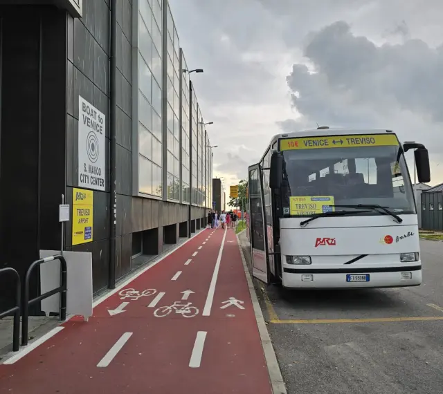 Autobus z napisem "Venice Treviso" czeka na pasażerów przy lotnisku. Obok czerwona ścieżka rowerowa i piesza.