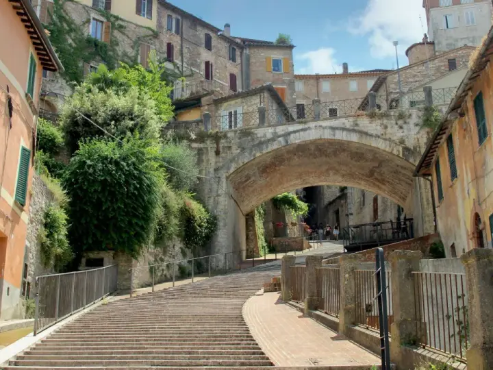 Perugia co zobaczyć: malownicze schody prowadzące pod zabytkowy most, otoczone kamiennymi domami i zielenią.