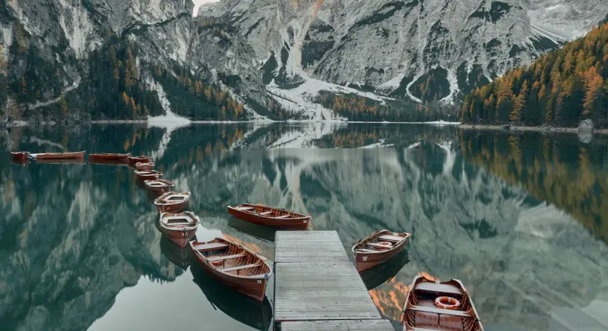 Drewniane łodzie przy drewnianym pomoście na spokojnym Lago di Braies, odbijające się w tafli wody, z majestatycznymi górami w tle.
