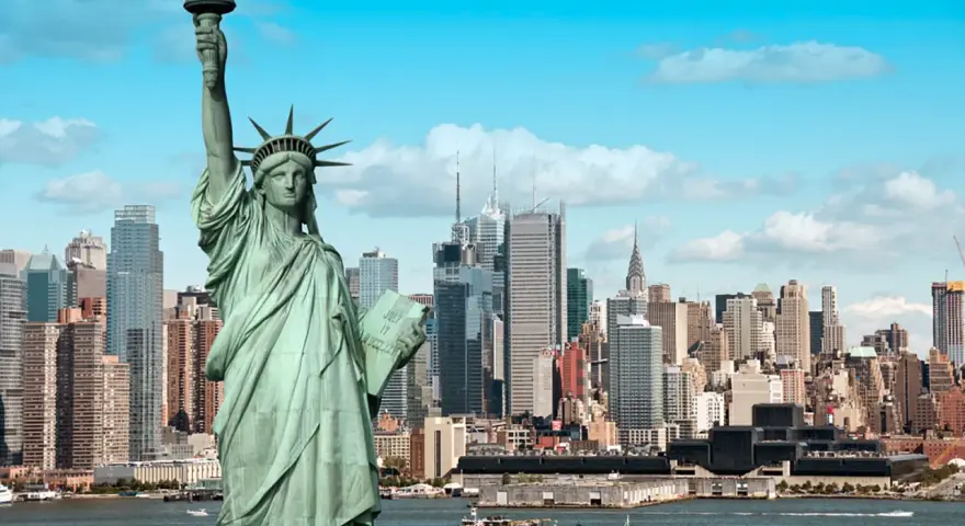 Statua Wolności wita podczas podróży do USA. W tle panorama Nowego Jorku z drapaczami chmur i statkami na rzece.